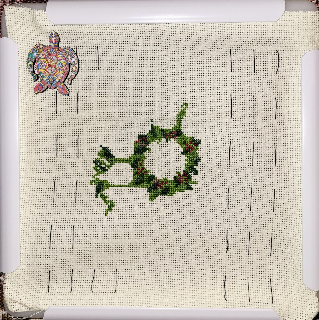 Christmas wreath cross stitch in progress - center ring complete, with light and dark green and finally some little red stitches